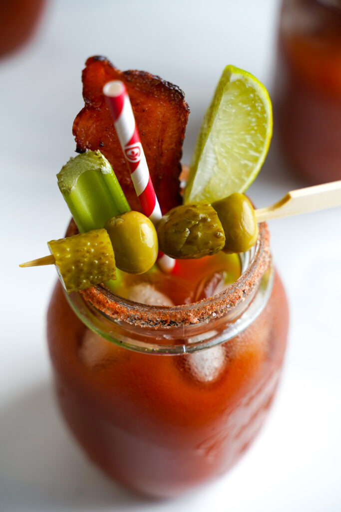 Canadian Caesar cocktail with a spiced rim garnished with celery and a bacon slice