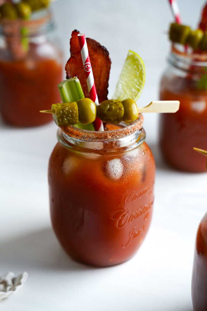Canadian Caesar cocktail in a mason jar glass, spiced rim and garnished with celery, pickle and bacon slice