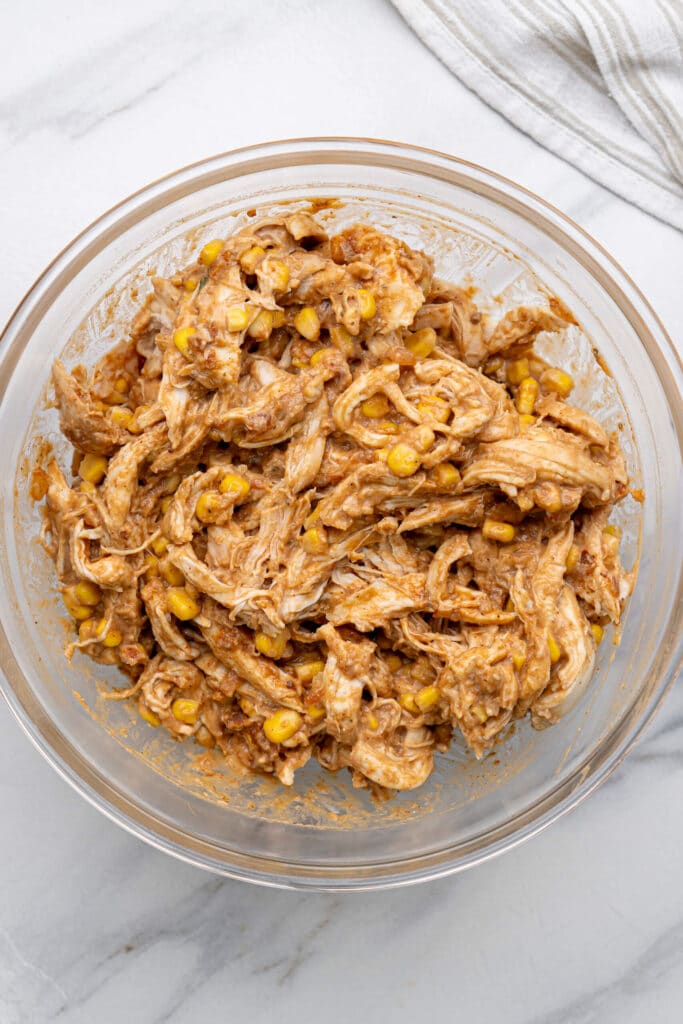 Shredded chicken, corn, refried beans, sour cream and salsa mixed together in a bowl for sheet pan chicken quesadillas