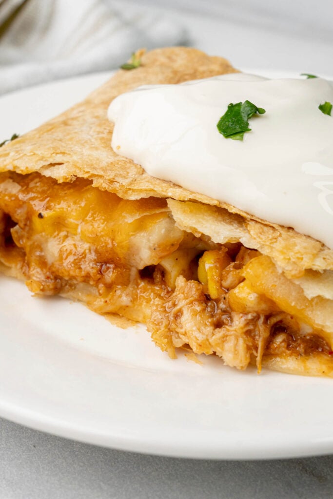 Close-up of a chicken quesadilla with melted cheese and shredded chicken, topped with a dollop of sour cream and fresh cilantro