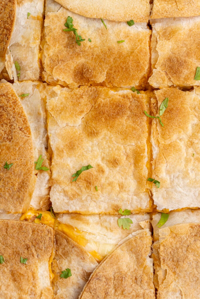 Close-up of crispy sheet pan quesadillas, sliced into squares and garnished with fresh cilantro