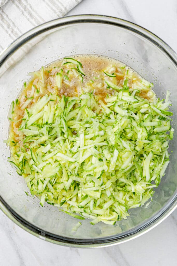 Grated zucchini mixed into wet muffin batter in a glass bowl for zucchini chocolate chip muffins.
