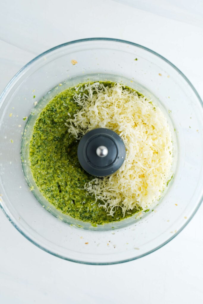 Freshly grated Parmesan cheese added to the blended pesto mixture in a food processor