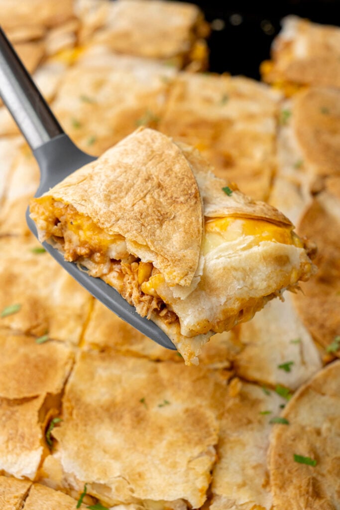 Sheet pan chicken quesadillas sliced with melted cheese, refried beans, and shredded chicken being served on a serving turner