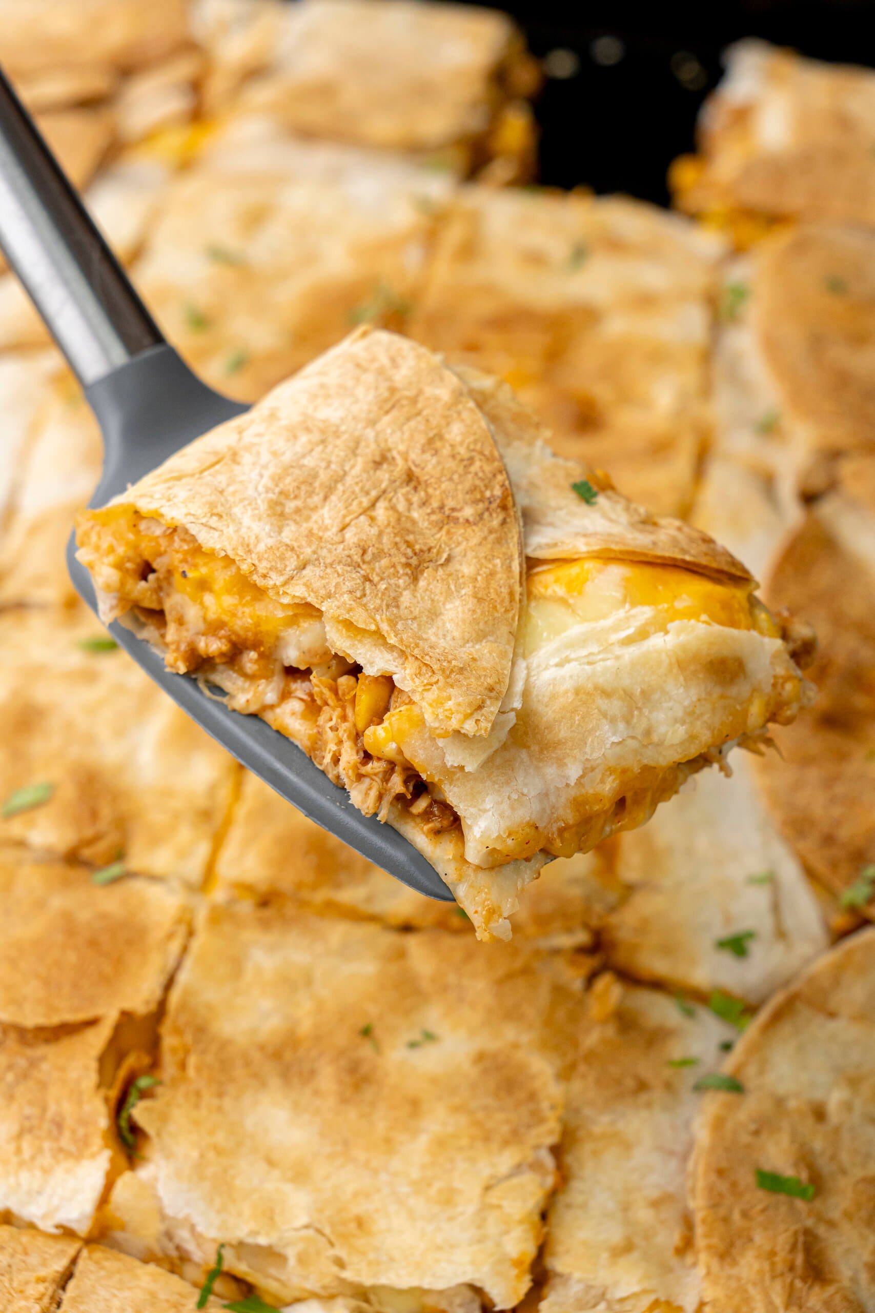 Sheet pan chicken quesadillas sliced with melted cheese, refried beans, and shredded chicken being served on a serving turner