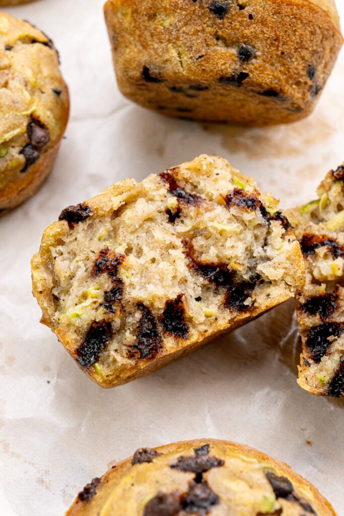 Close-up of a halved zucchini chocolate chip muffin showing a soft, moist interior with melty chocolate chips and flecks of green zucchini.