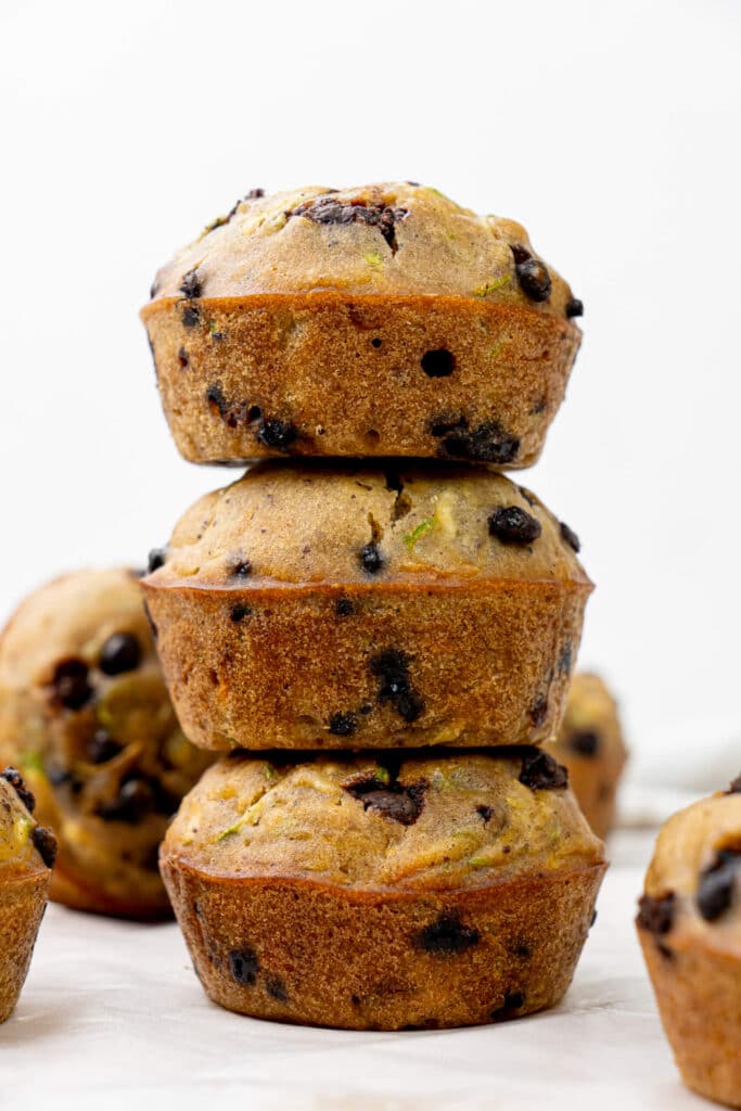 Close-up of stacked zucchini chocolate chip muffins with golden edges, chocolate chips, and flecks of zucchini.