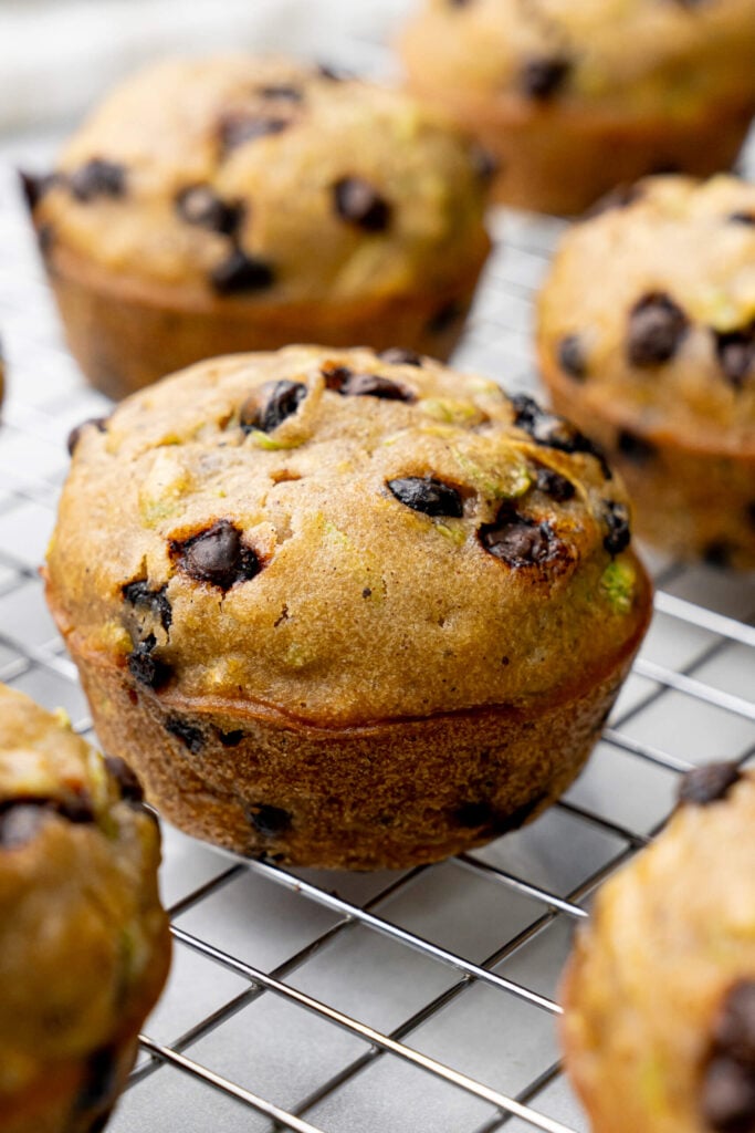 Close-up of freshly baked zucchini chocolate chip muffins cooling on a wire rack, showing golden tops and gooey chocolate chips.