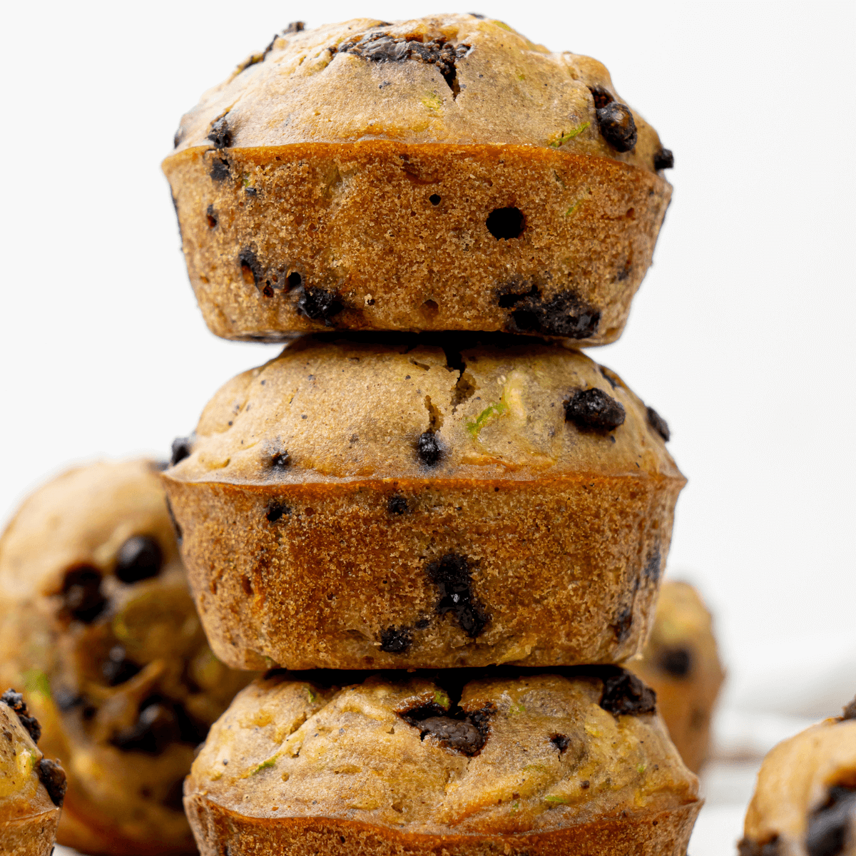 Zucchini chocolate chip muffins stacked on top of each other, showing golden edges and melty chocolate chips.