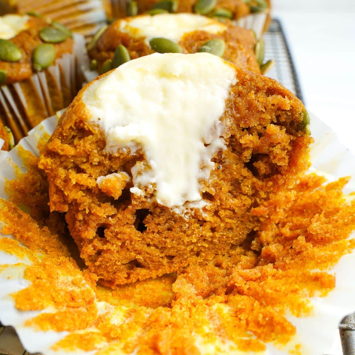 Close-up of a pumpkin muffin with a creamy cream cheese center and pumpkin seeds on top.