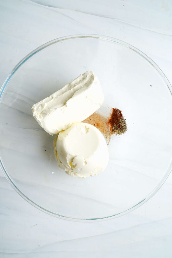 Cream cheese, sour cream, cayenne, salt, and pepper in a mixing bowl ready to be blended.