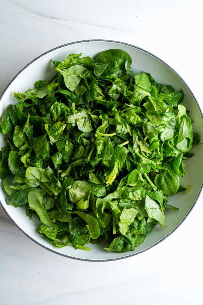 Skillet filled with roughly chopped fresh spinach.