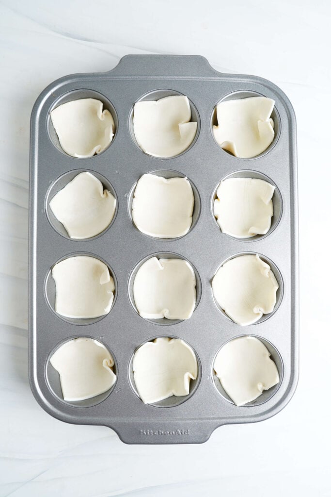 A muffin tin filled with puff pastry squares pressed into each cup, ready for filling.