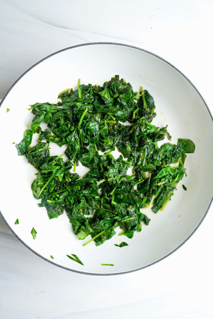 Spinach wilted in a skillet after sautéing to remove excess moisture.