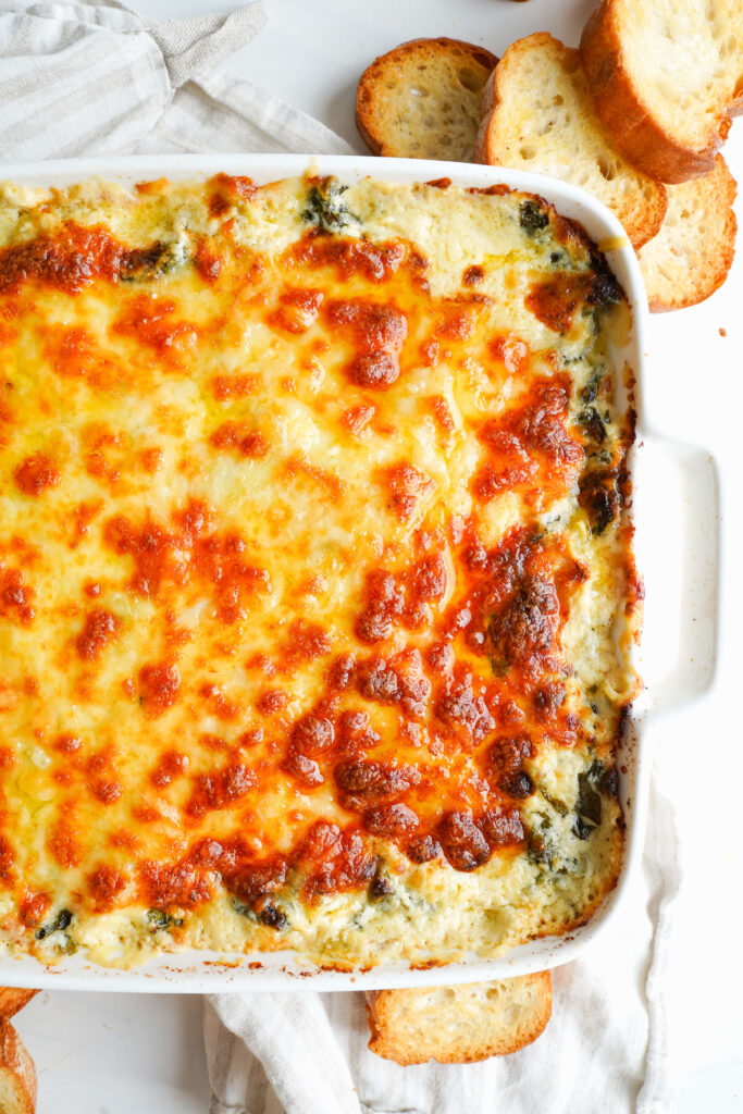 Close-up of golden, bubbly spinach artichoke dip fresh from the oven.