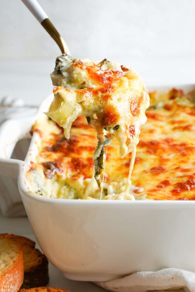 Spoon lifting creamy spinach artichoke dip with melted, golden cheese.