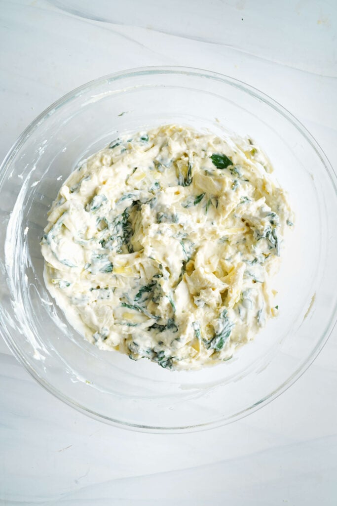 Creamy spinach and artichoke dip mixture combined in a glass bowl before baking.