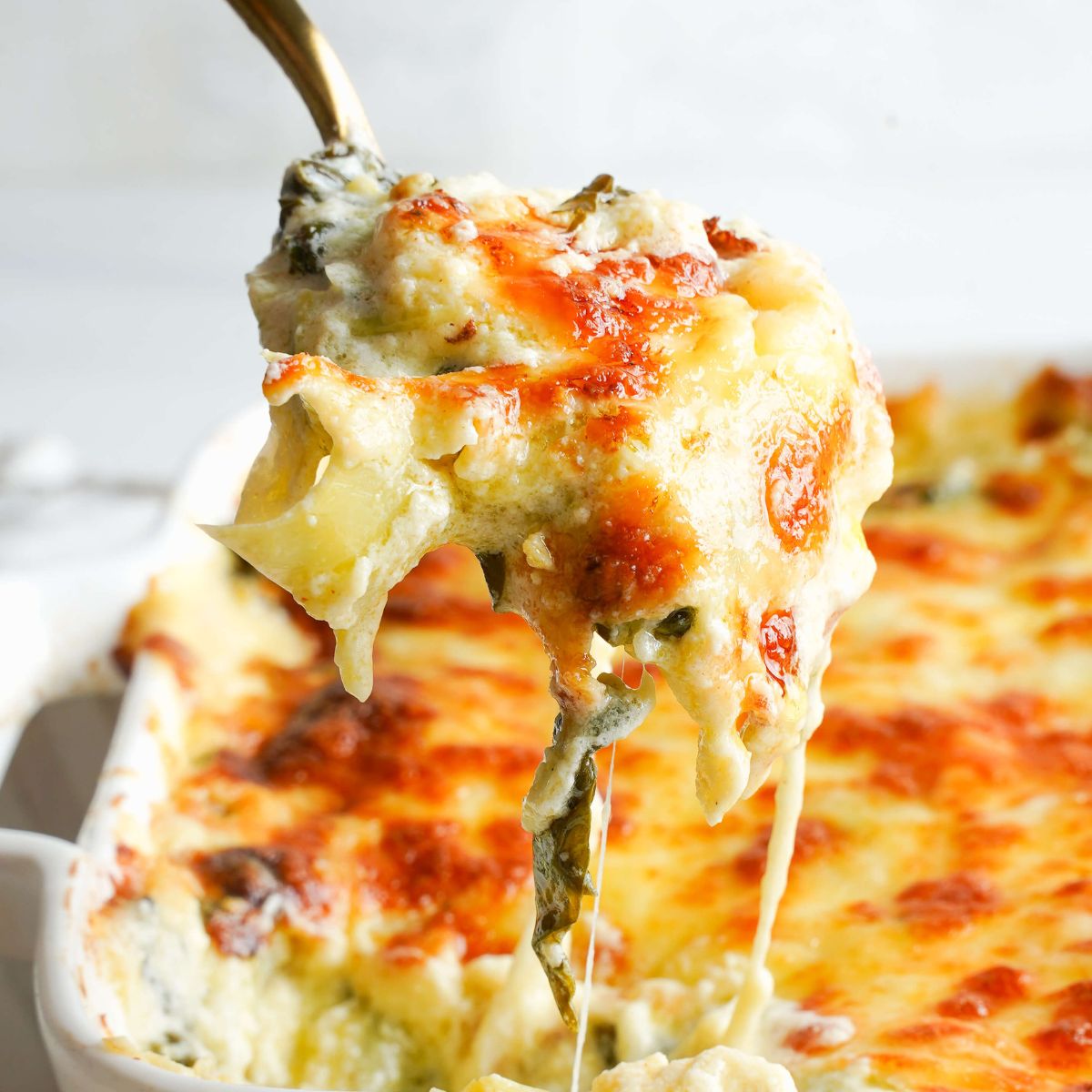 Cheesy spinach artichoke dip being lifted with a spoon.