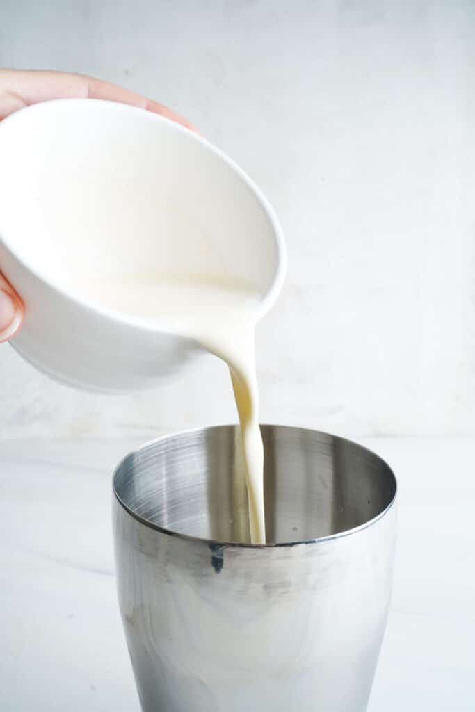 Eggnog being poured into a metal cocktail shaker