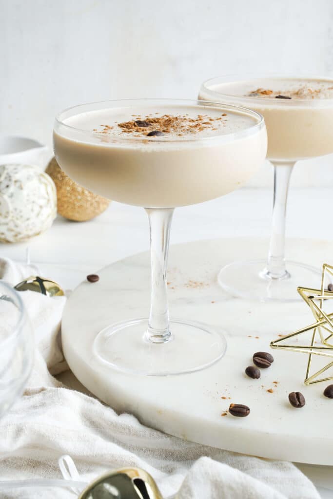 Eggnog espresso martini made with espresso, eggnog, spiced rum, and coffee liqueur, served in coupe glasses with a cinnamon garnish