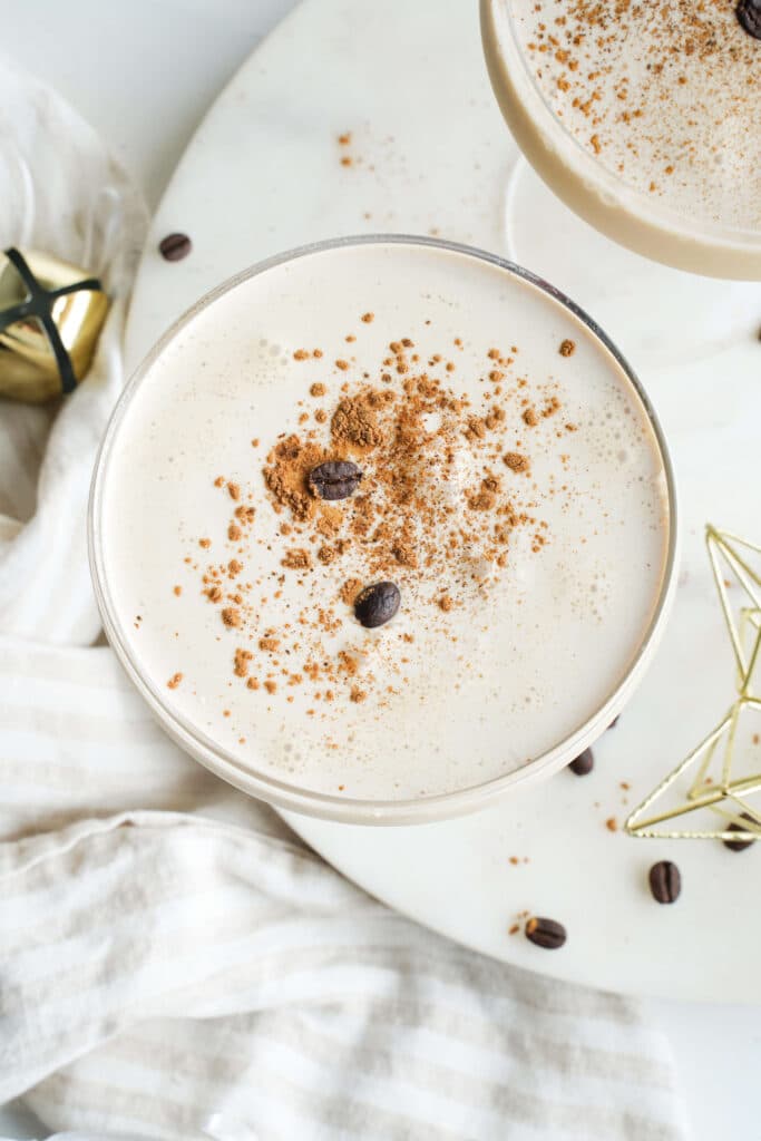 Top view of an eggnog espresso martini with espresso crema, cinnamon, and coffee beans in a coupe glass