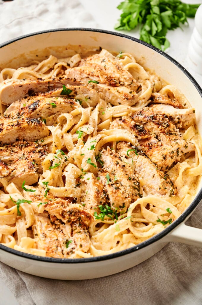 Garlic parmesan chicken and pasta with sliced seasoned chicken over creamy fettuccine in a skillet.