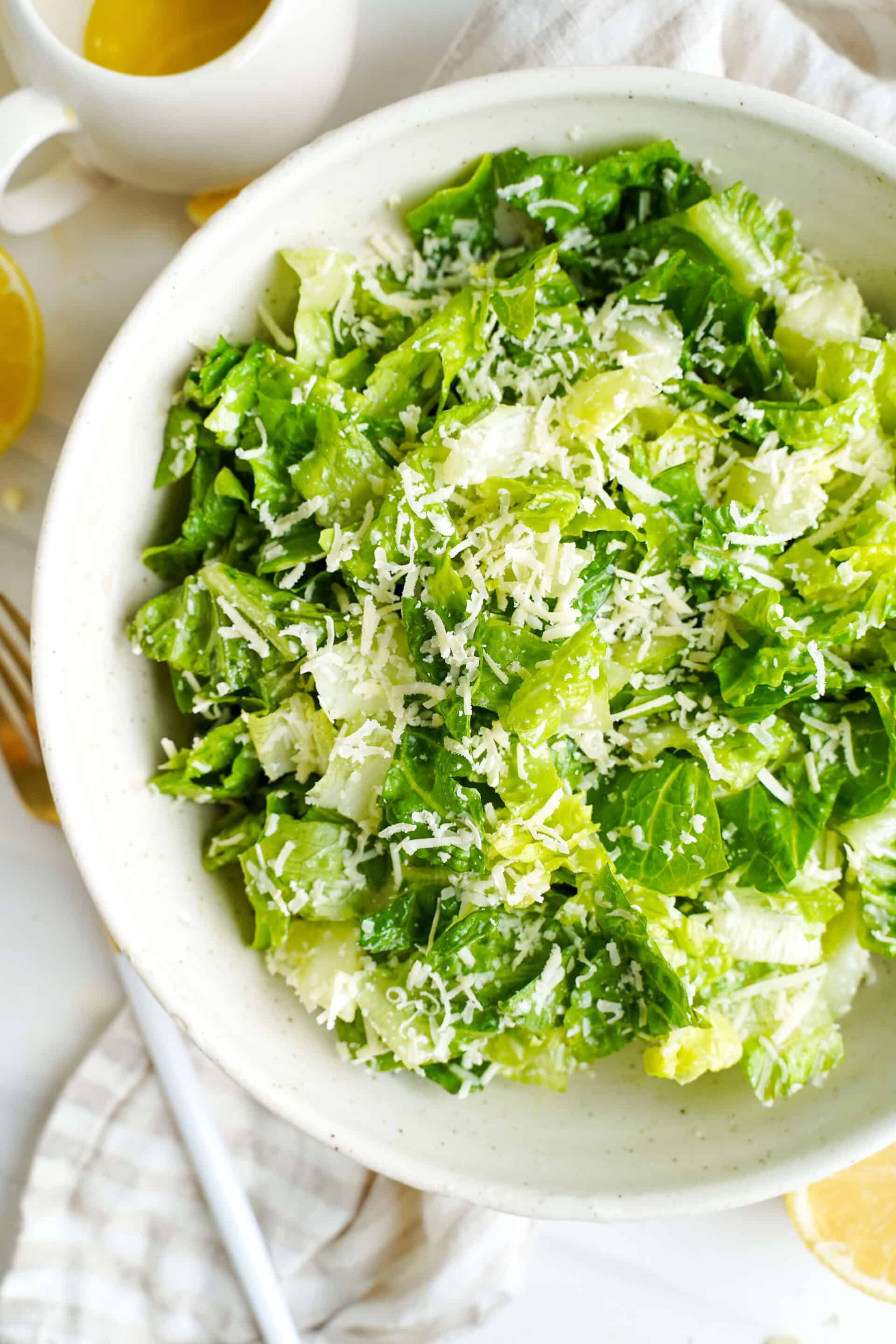 Bowl of chopped romaine lettuce topped with finely grated Parmesan cheese, with a lemon half and white pitcher nearby