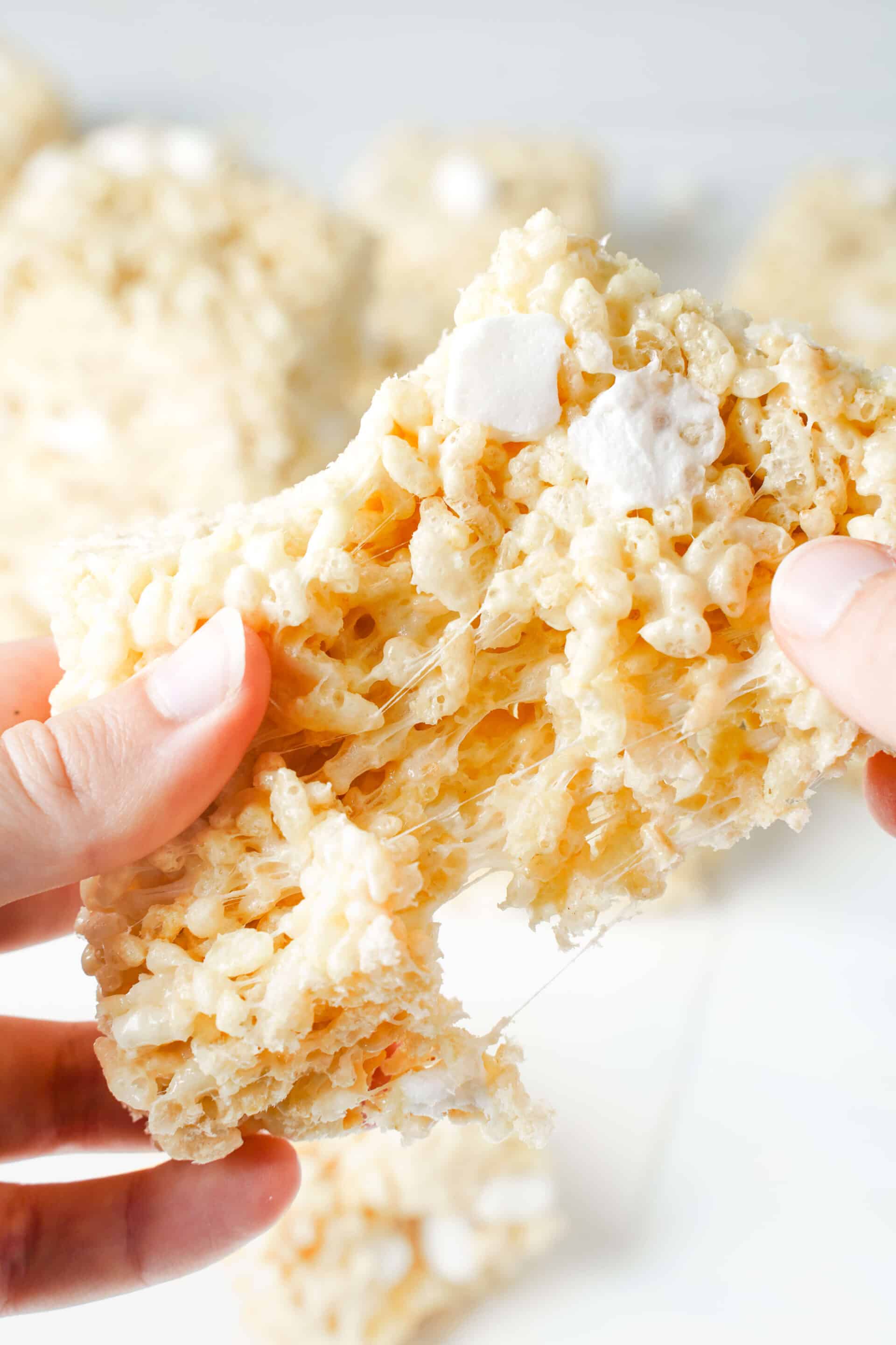 Hands pulling apart a gooey Rice Krispie treat with melted marshmallow stretching between the cereal and soft marshmallow pockets visible throughout.