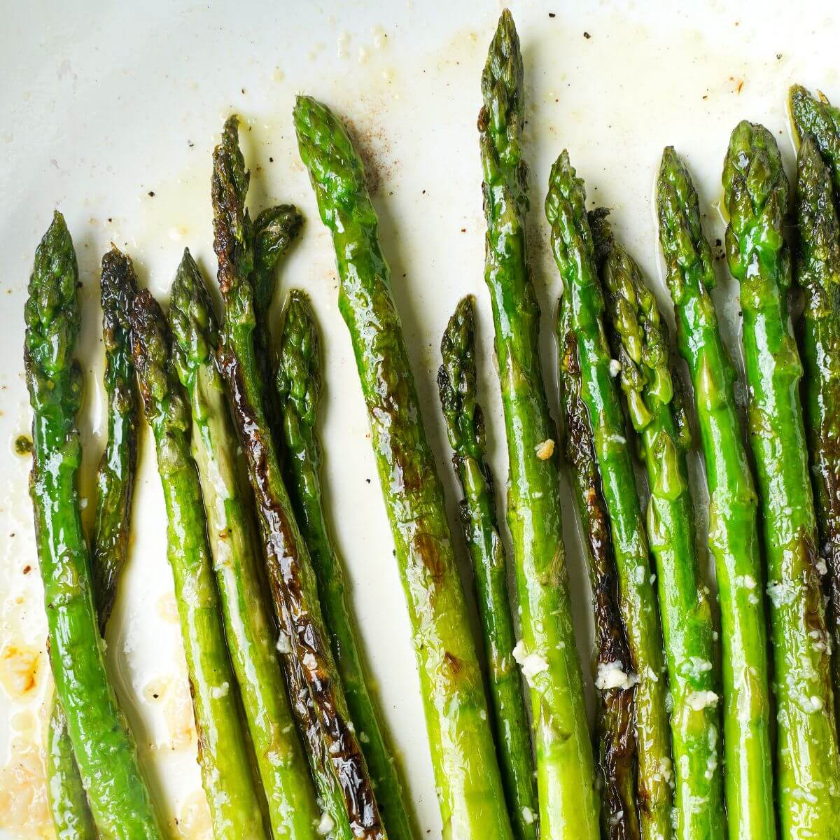 Sautéed asparagus spears in a skillet with olive oil, garlic, black pepper, and lightly charred edges.