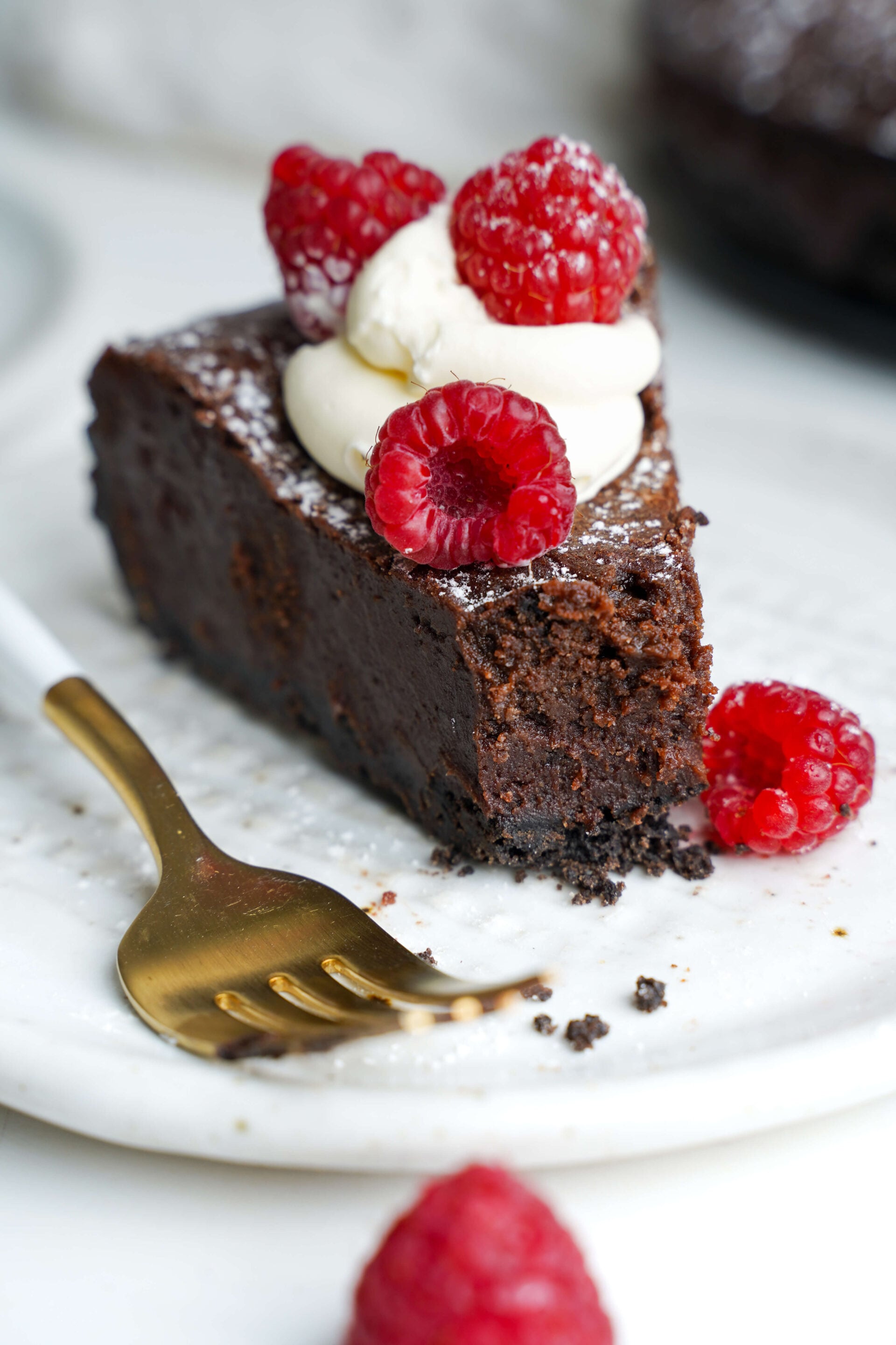 Slice of flourless chocolate torte topped with whipped cream and fresh raspberries