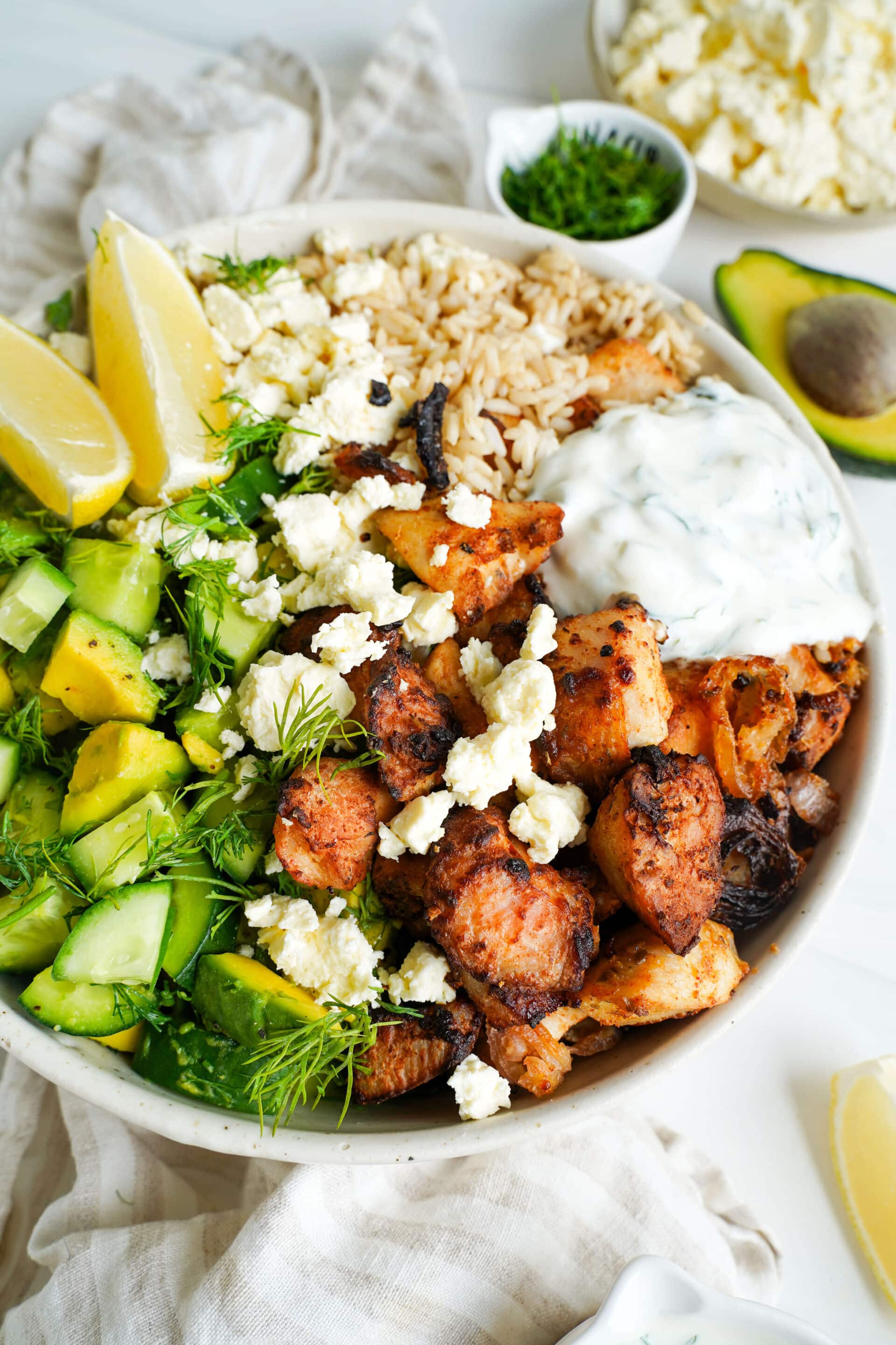 Greek chicken bowl with seasoned chicken, cucumber avocado salad, feta cheese, rice, tzatziki and fresh dill.