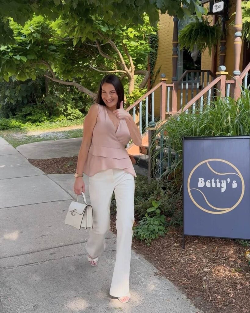 Cassandra walking in front of Betty's with a Betty's sign in front of greenery.