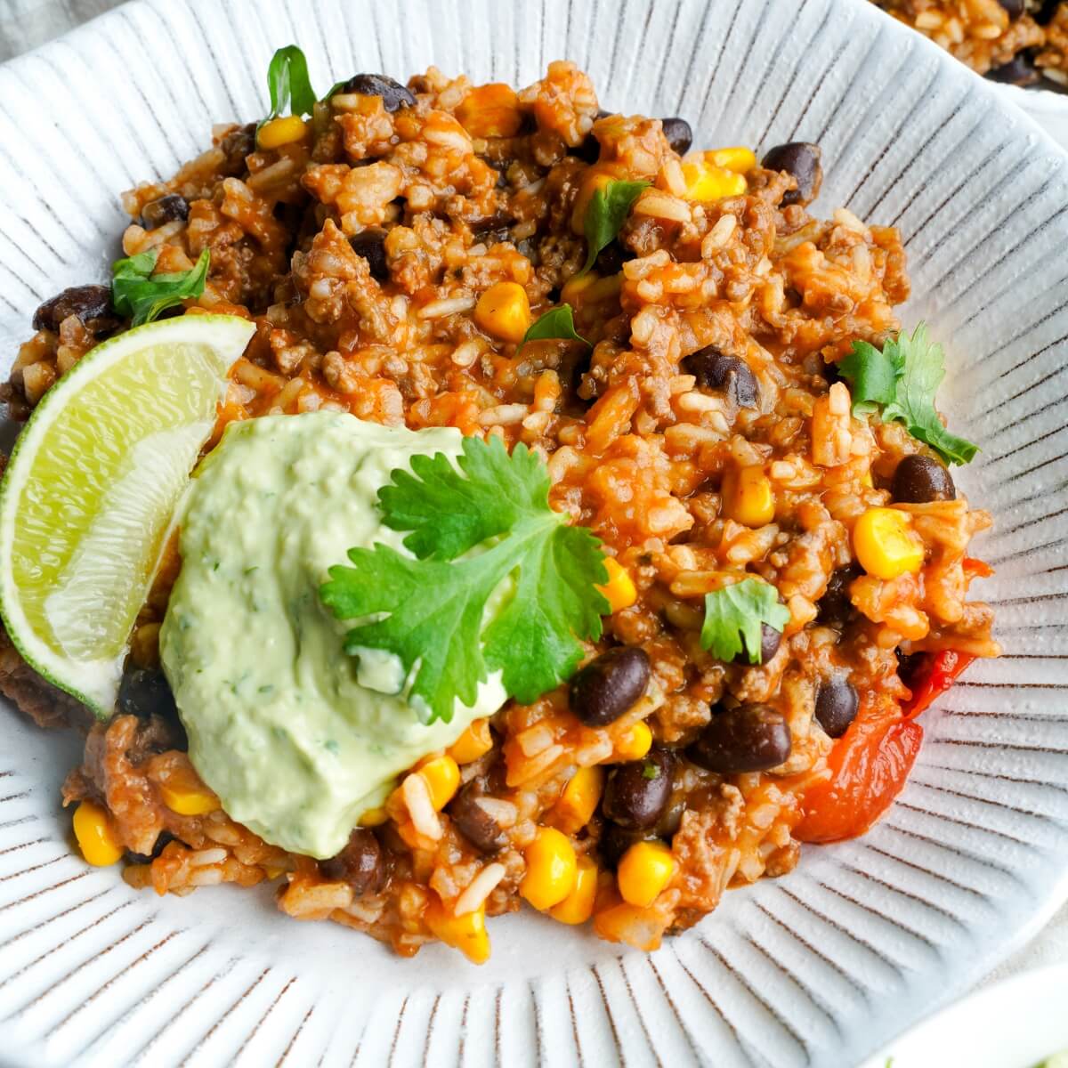 Easy taco rice bowl topped with avocado lime crema, fresh cilantro, and a lime wedge