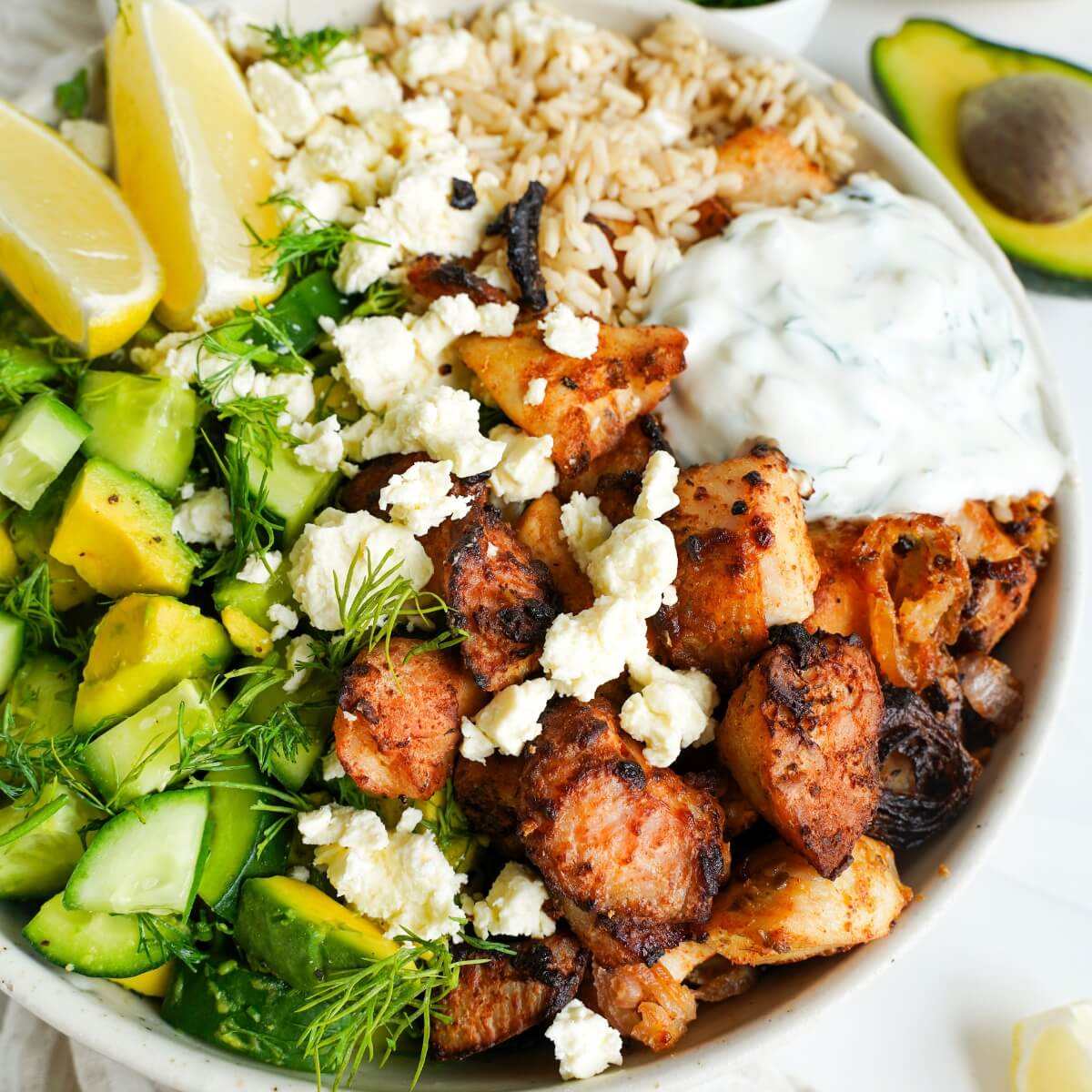 Greek Chicken Bowls recipe with brown rice, cucumber avocado salad, feta and tzatziki