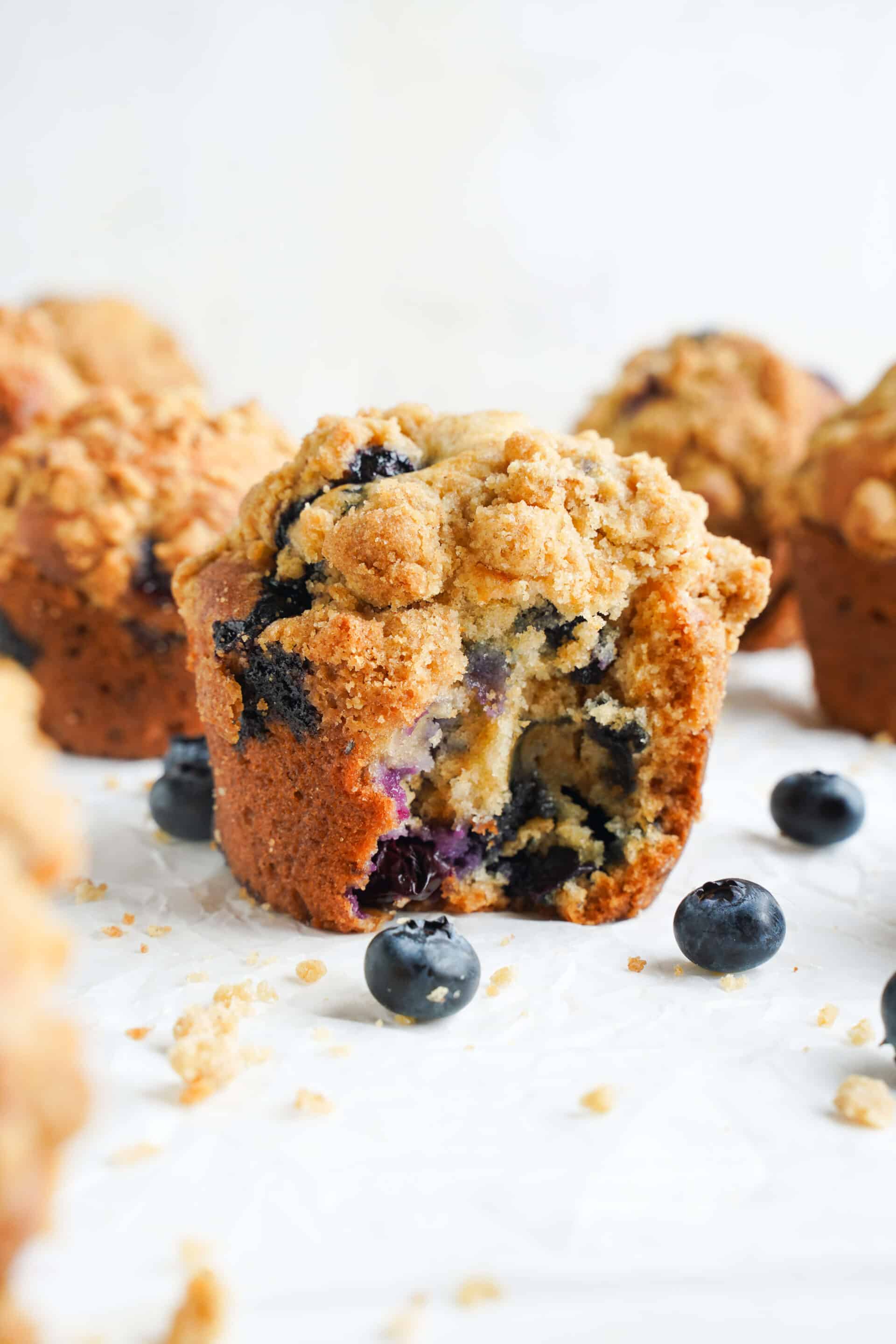 Homemade blueberry muffin with a golden cinnamon streusel topping, broken open to reveal a soft center filled with fresh blueberries.