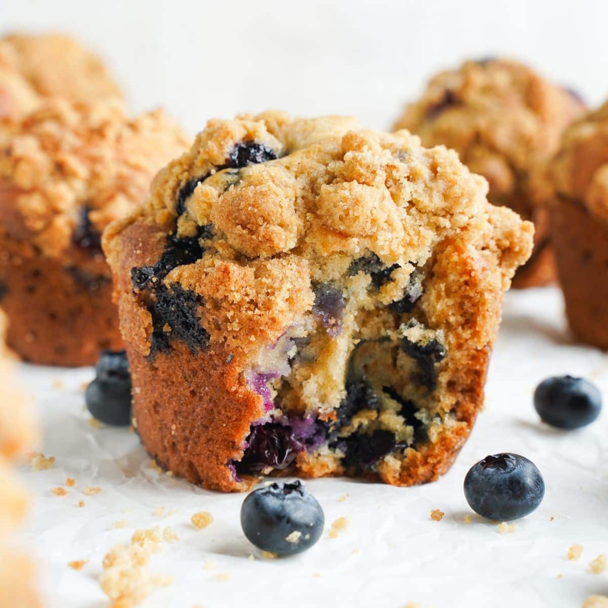 Homemade blueberry muffin with golden cinnamon streusel topping, broken open to show a soft center filled with juicy blueberries.